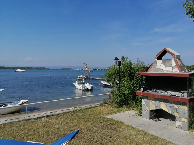 Stone barbecue on the waterfront lawn with a boat moored behind